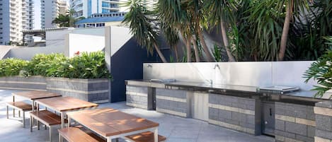 Een terras buiten met een barbecue, zitplaatsen en planten.
