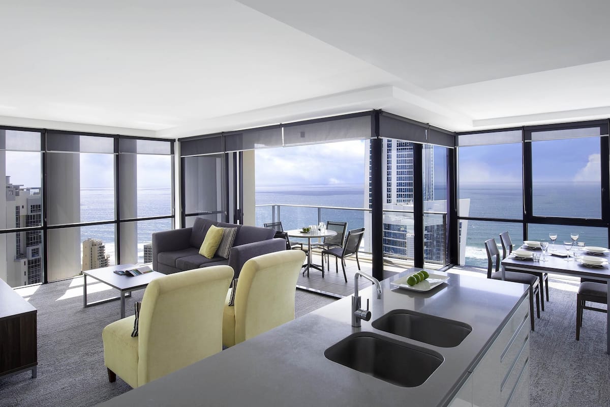 A modern kitchen with a large island, a dining area with a view of the ocean, and a seating area with a sofa and chairs.
