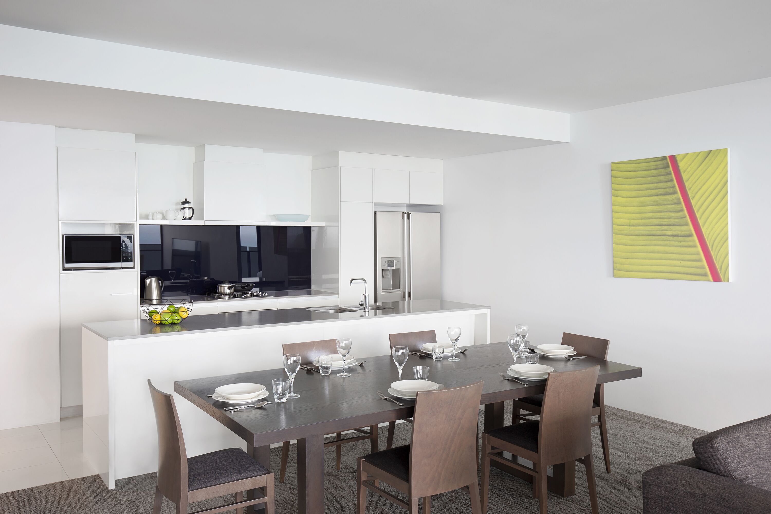 Une cuisine moderne avec des meubles blancs, un îlot central et un coin repas comprenant une table et des chaises en bois foncé.