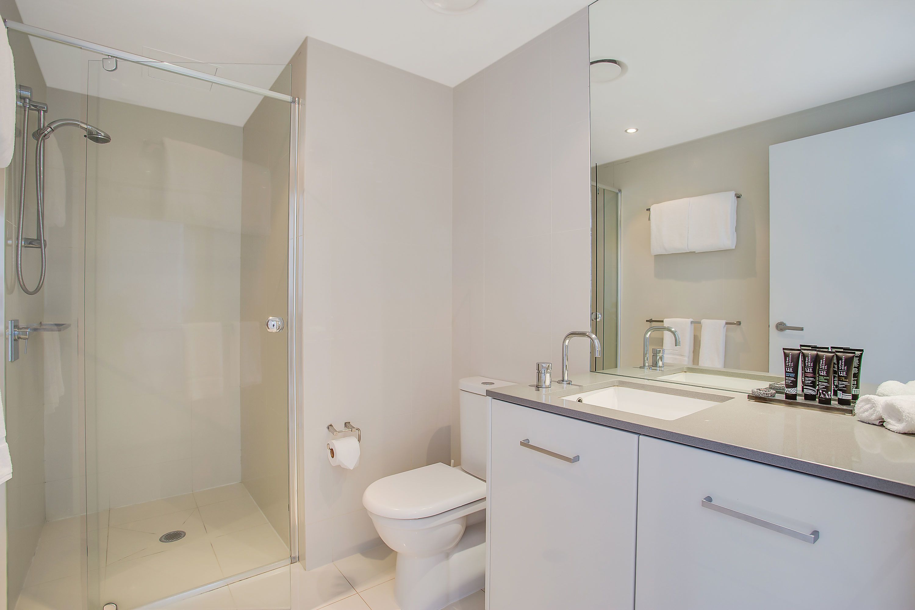 A modern bathroom with a glass-enclosed shower, a toilet, a sink with a mirror, and a cabinet with drawers.
