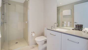 A modern bathroom with a glass-enclosed shower, a toilet, a sink with a mirror, and a cabinet with drawers.