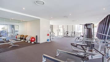 A modern gym with various exercise equipment, a mirrored wall, and a large window providing natural light.
