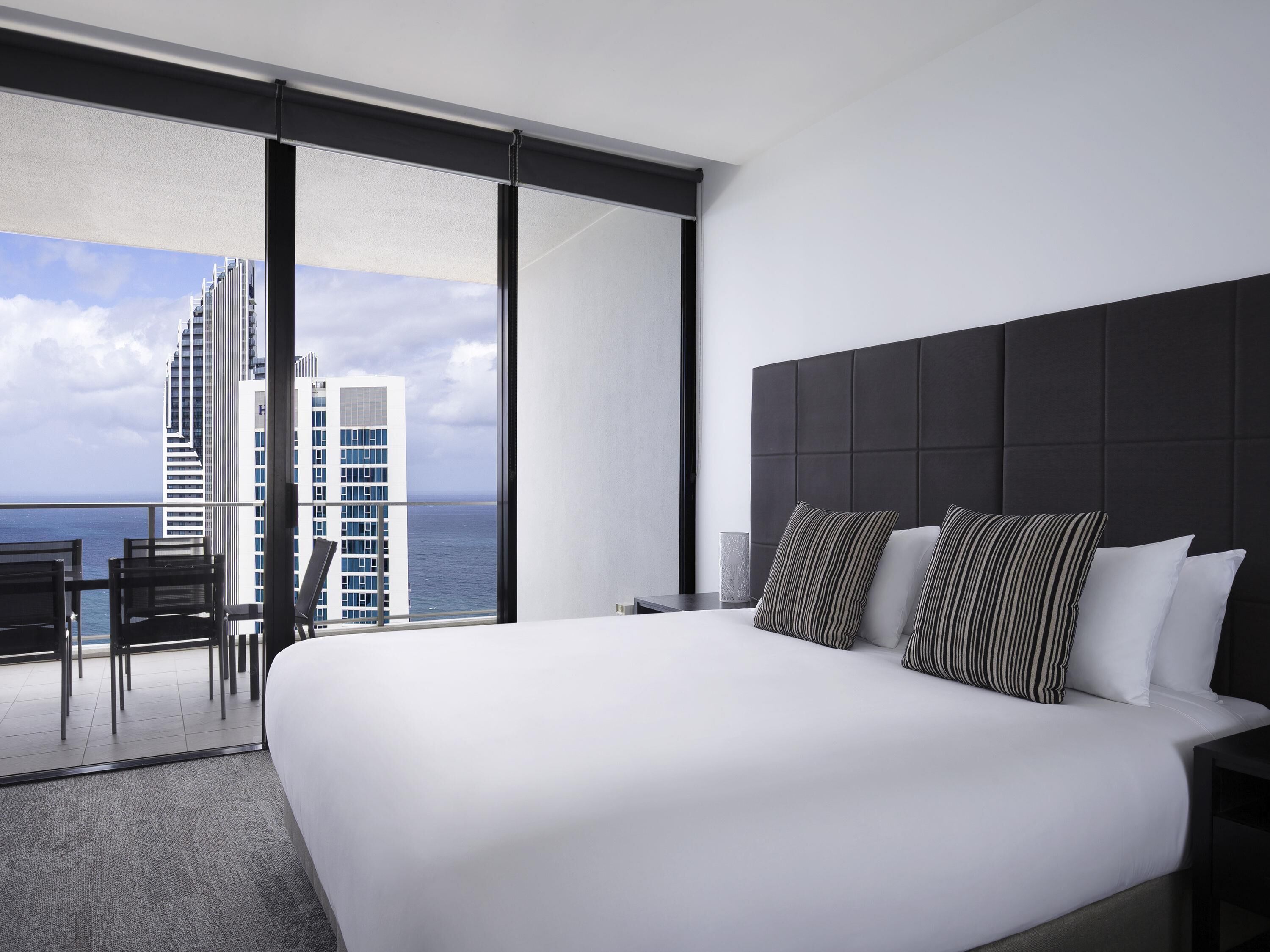 Ein modernes Hotelzimmer mit einem großen Bett, Meerblick und einem Balkon mit Sitzgelegenheiten.