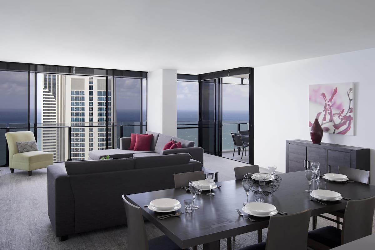 A modern dining area with a table set for four, a sofa, and a balcony with a city view.