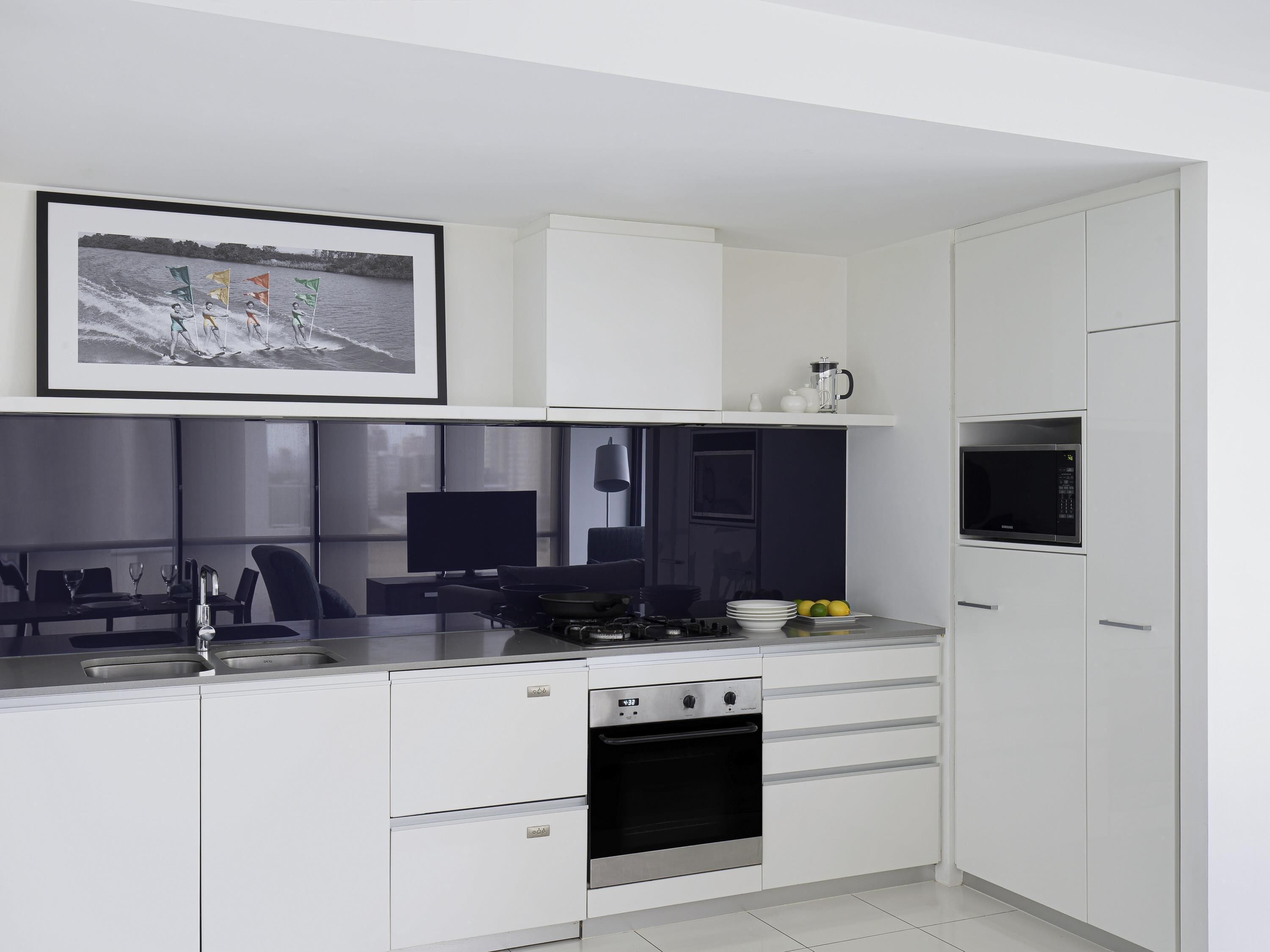 A modern kitchen with white cabinetry, a built-in stove, a microwave, and a dining area with a TV.