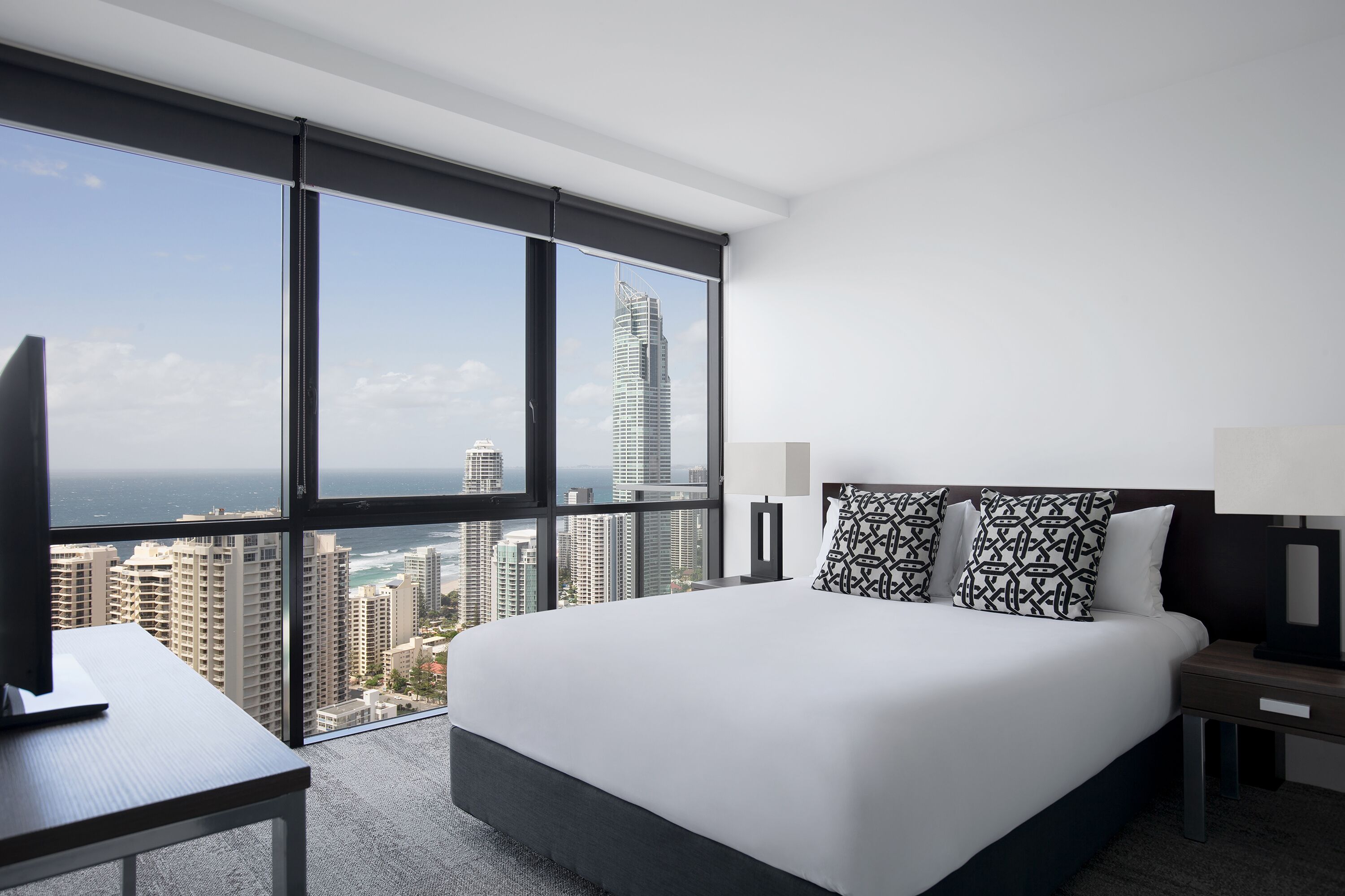 A modern hotel room with a large bed, a desk, and a view of a city skyline.