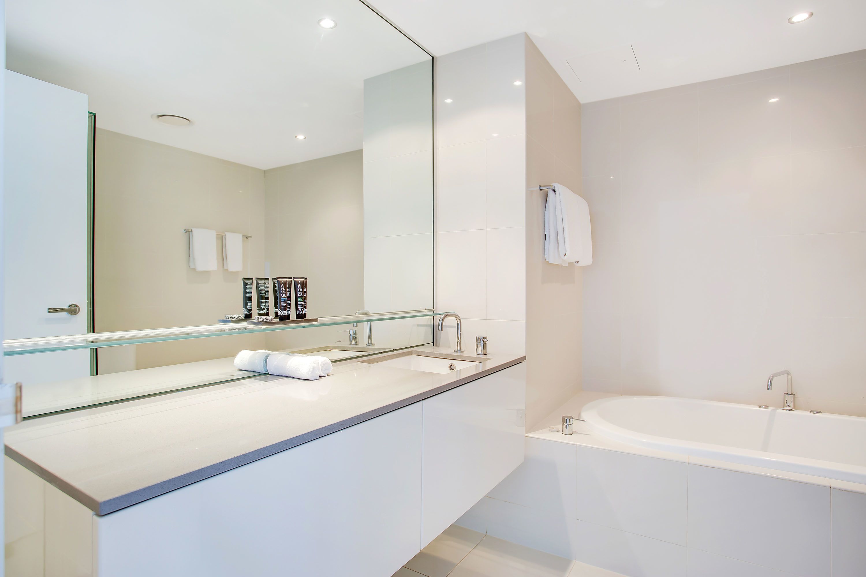 A modern bathroom with a large mirror, a bathtub, and a countertop with toiletries.