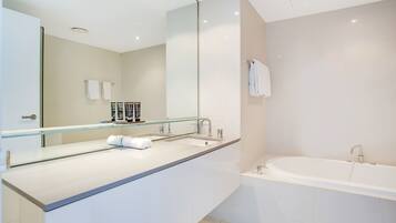 Une salle de bain moderne avec un grand miroir, une baignoire et un plan de toilette où sont posés les articles de toilette.