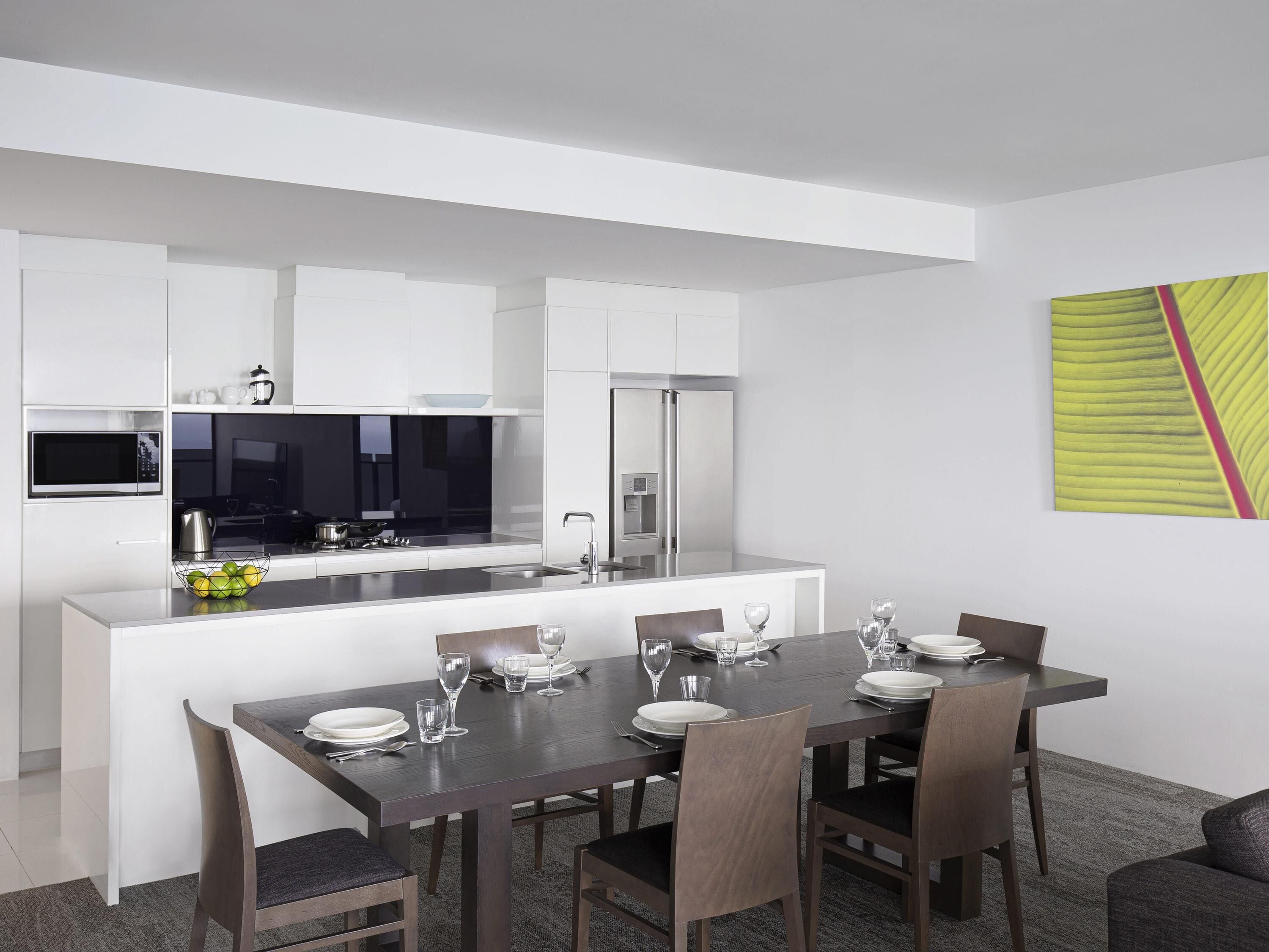 A modern kitchen with white cabinets, a microwave, and a dining area with a dark wooden table and chairs.