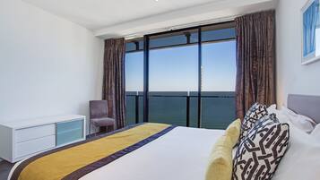 Ein Hotelzimmer mit einem großen Bett, einem Nachttisch, einem Sessel und Meerblick vom Balkon.