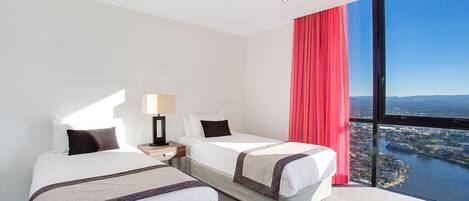 Habitación de hotel con dos camas, un ventanal grande con vistas a la ciudad y al agua, y una cortina roja.