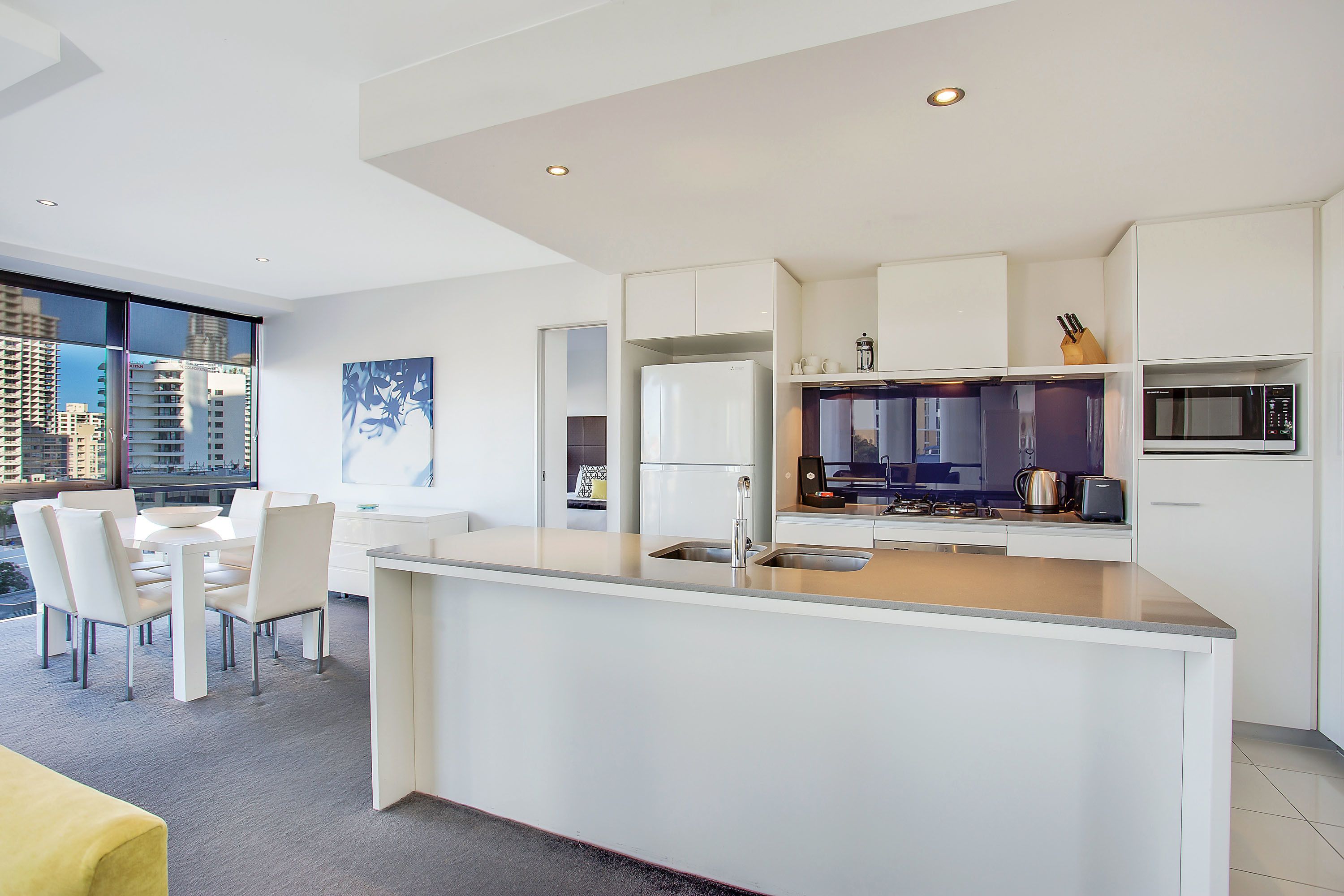 Una cocina moderna con armarios blancos, una isla central con pileta y un comedor con mesa y sillas.