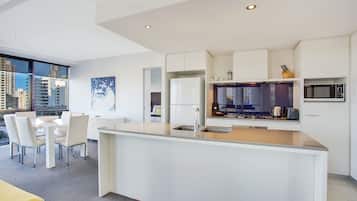 Una cocina moderna con armarios blancos, una isla central con pileta y un comedor con mesa y sillas.