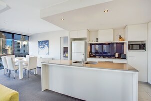 A modern kitchen with white cabinetry, a central island with a sink, and a dining area with a table and chairs.