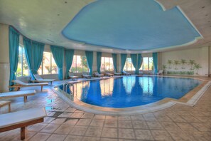 Una piscina cubierta, una piscina al aire libre, sombrillas, tumbonas