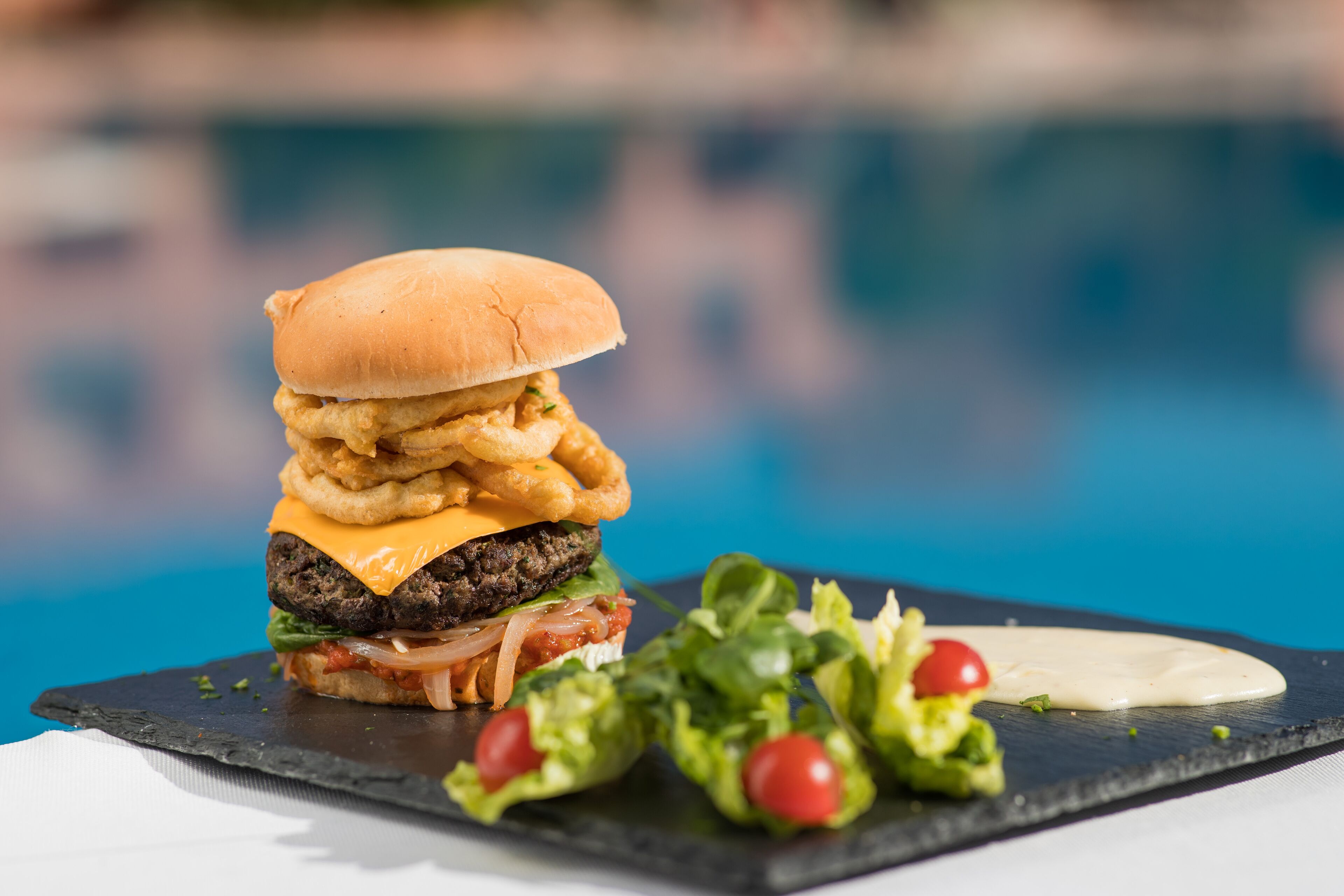 A burger with onion rings and a side salad on a slate plate.
