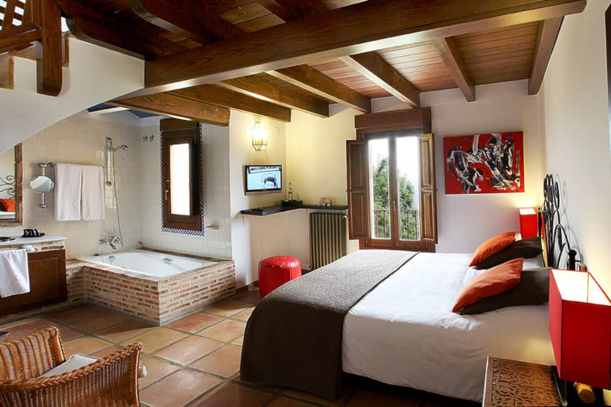 Une chambre avec un grand lit, une table de chevet rouge, une fenêtre avec vue, une salle de bain avec baignoire et un téléviseur fixé au mur.