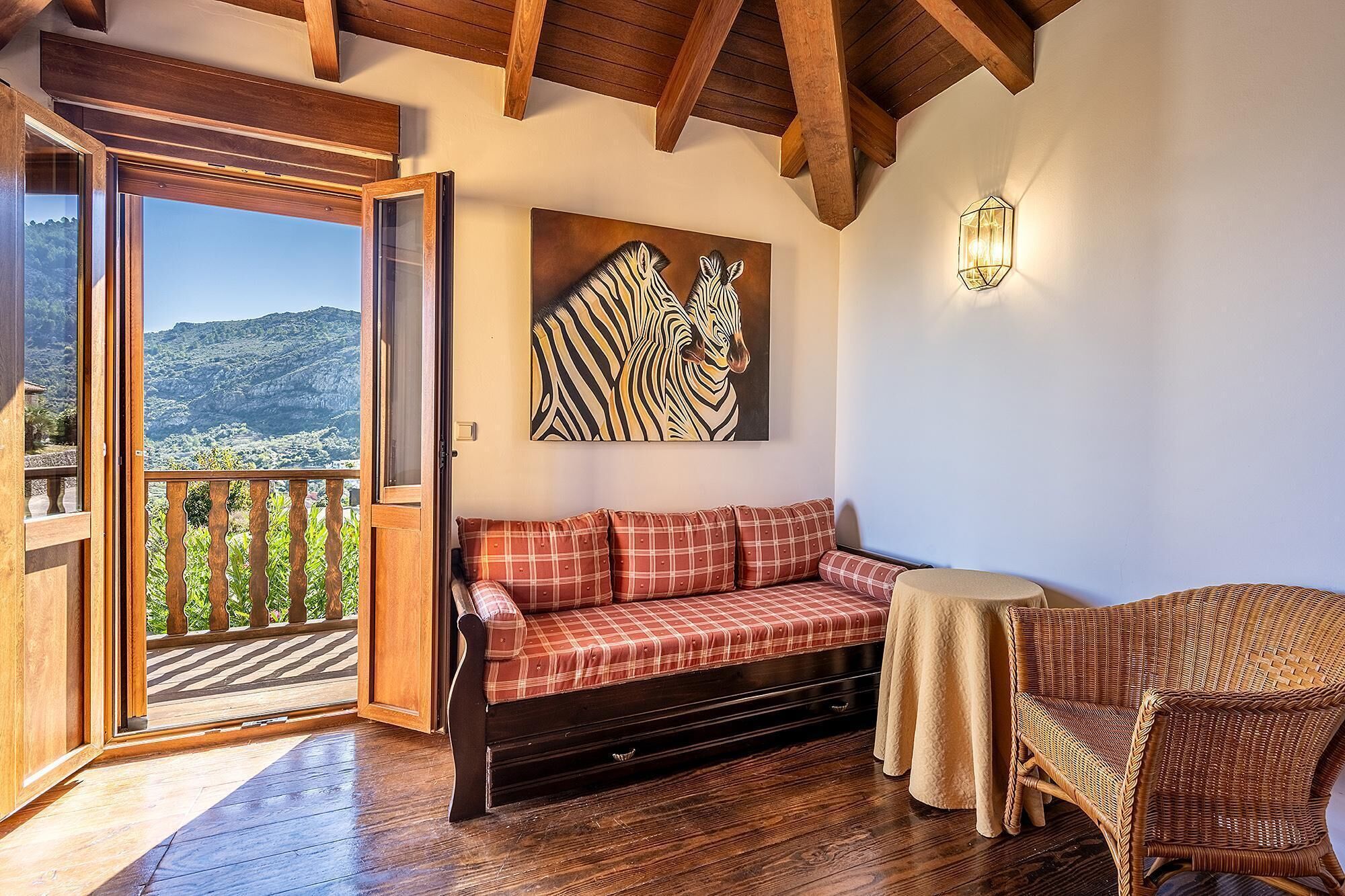 Una habitación acogedora con un banco de madera, una silla de mimbre y un amplio ventanal con vistas a un paisaje montañoso.