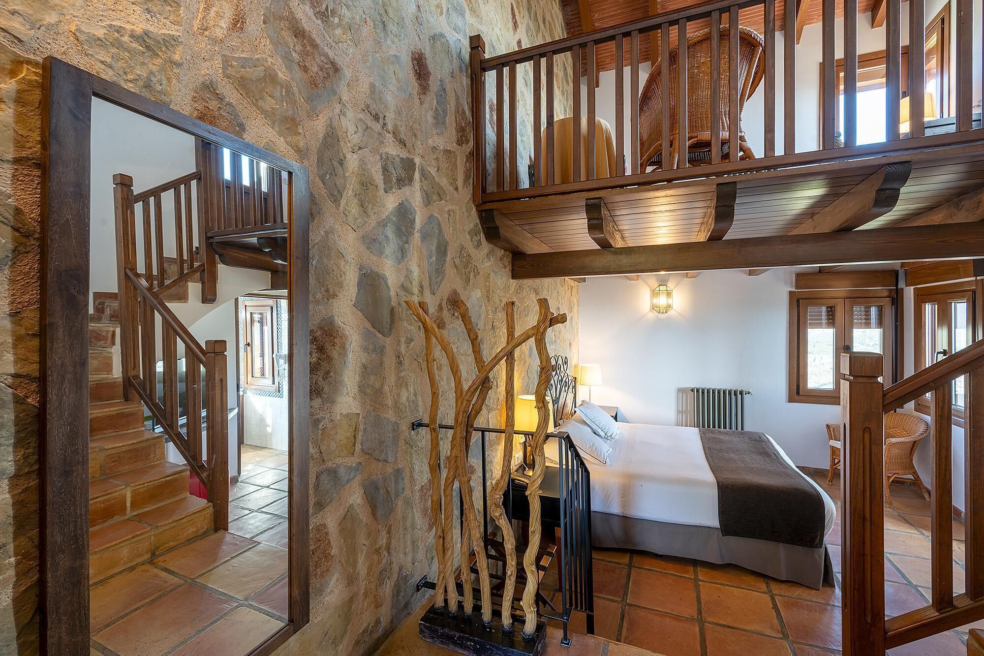 Um quarto com parede de pedra, escada de madeira e cama com cabeceira.