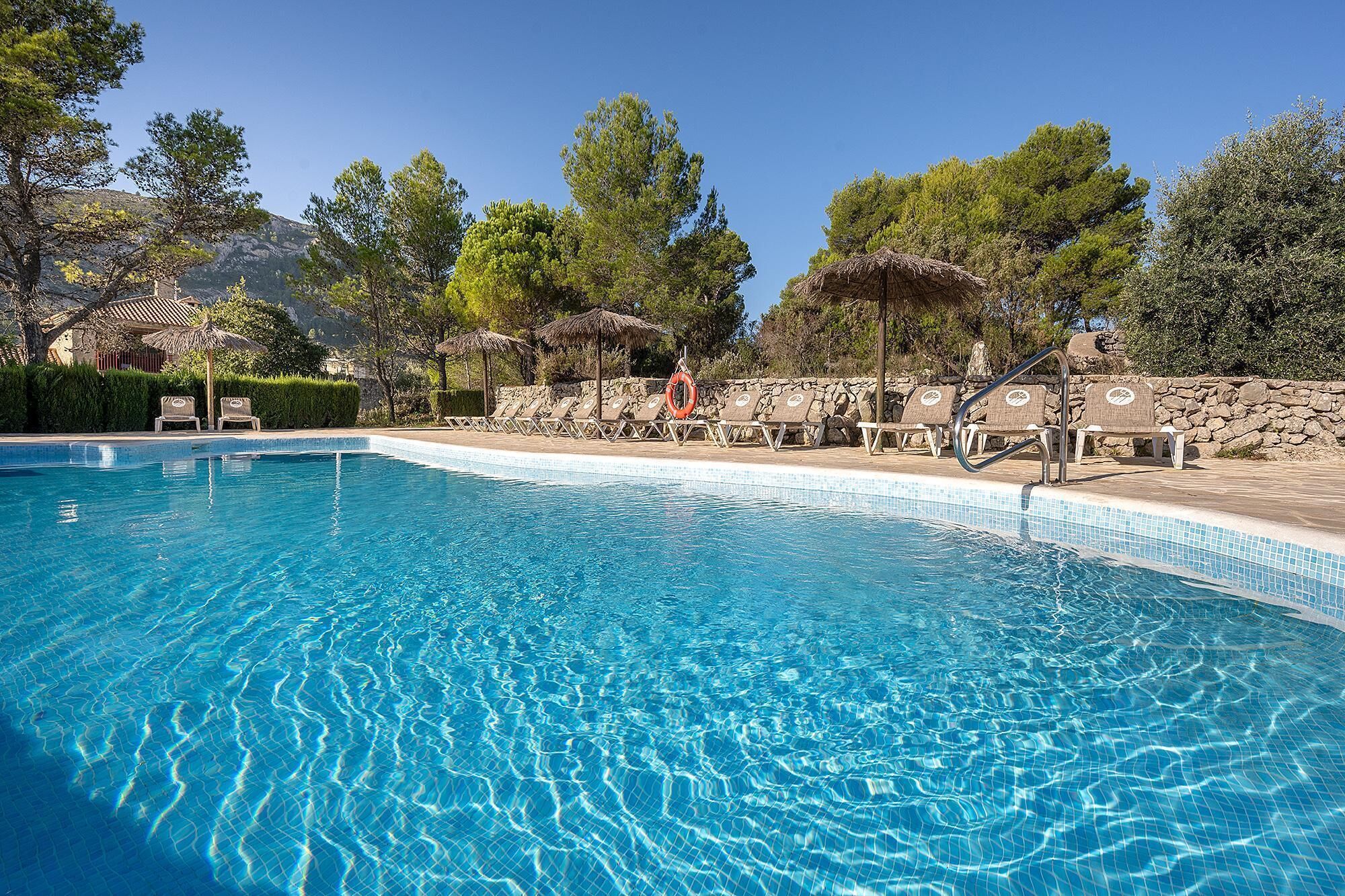 Una piscina azul cristalina con sillas de descanso y un muro de piedra.