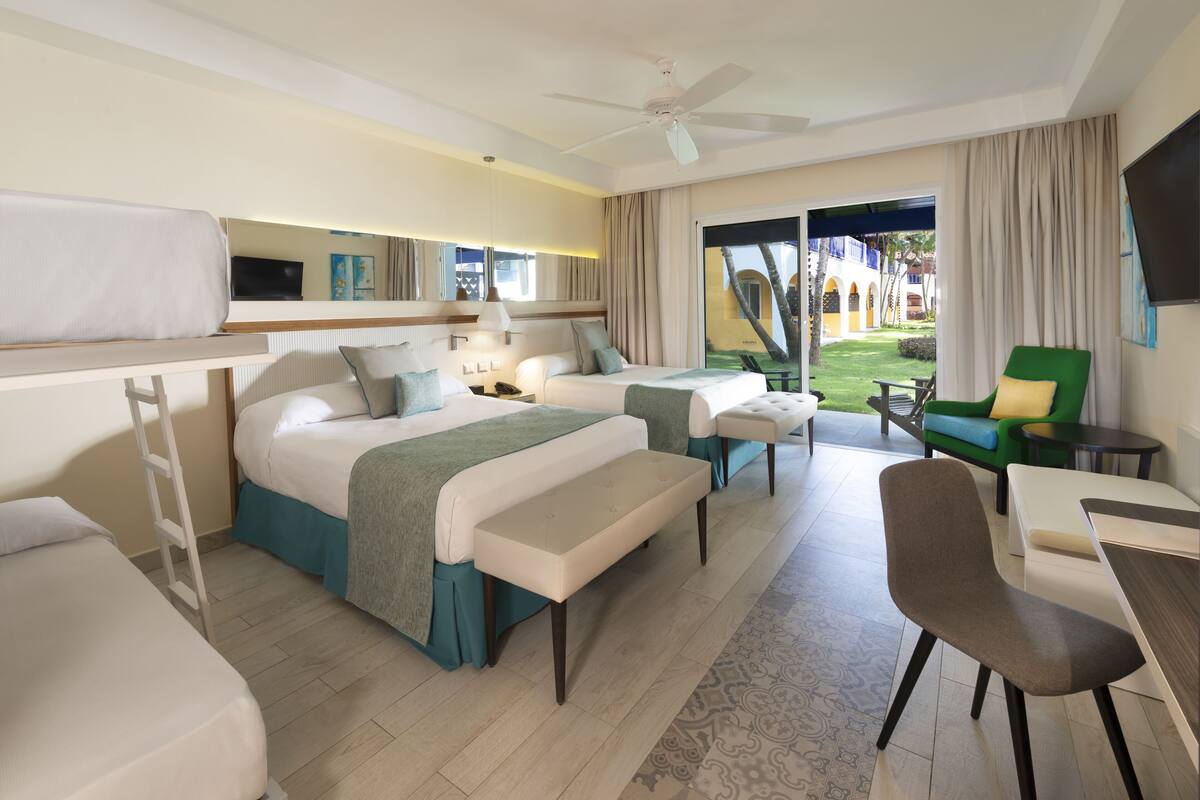 A hotel room with two beds, a desk, a chair, a TV, and a balcony with a view of the courtyard.