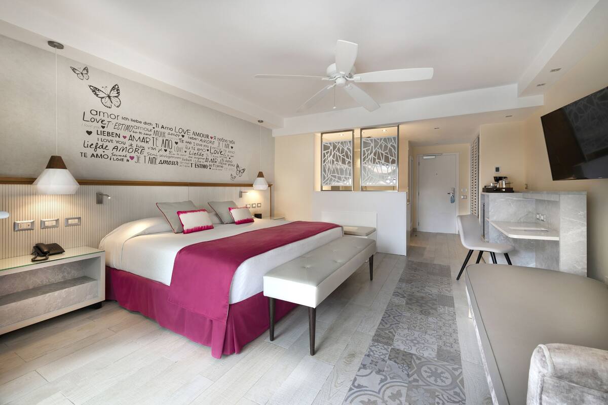 A modern bedroom with a bed, bedside tables, a desk, and a TV.