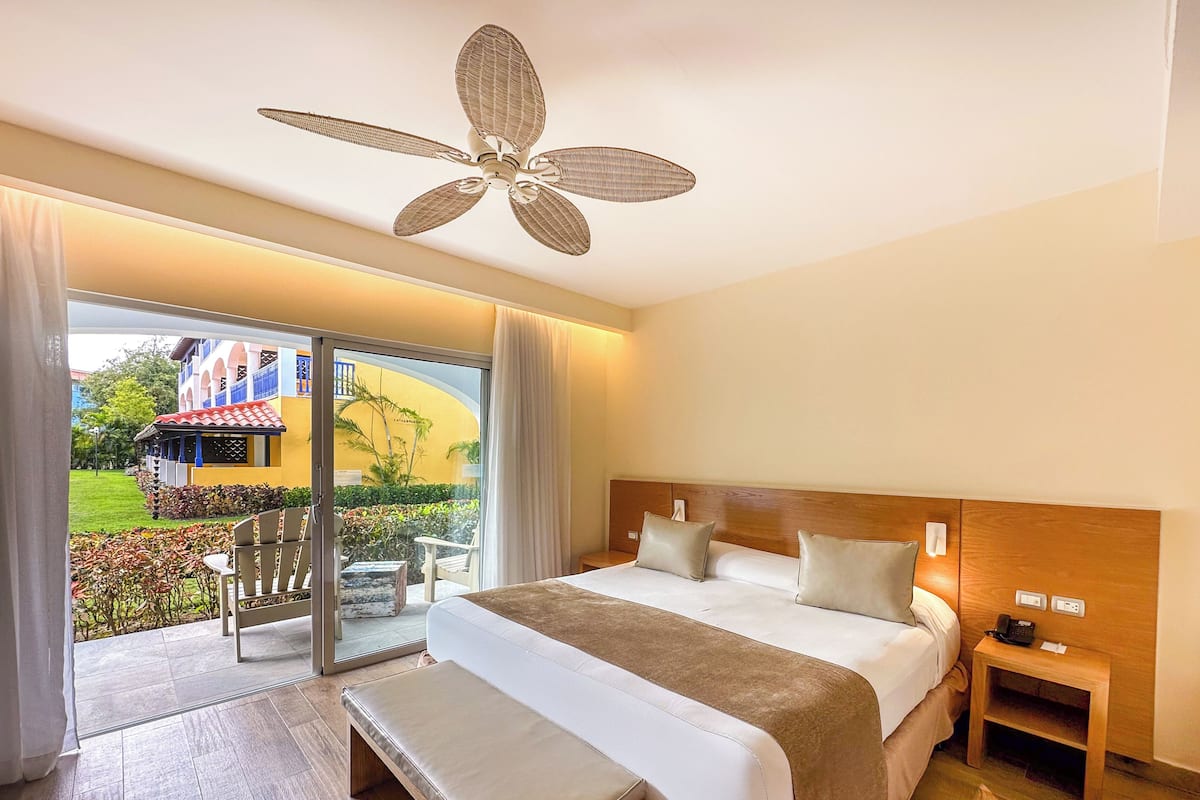 A hotel room with a bed, bedside table, bench, and a ceiling fan.