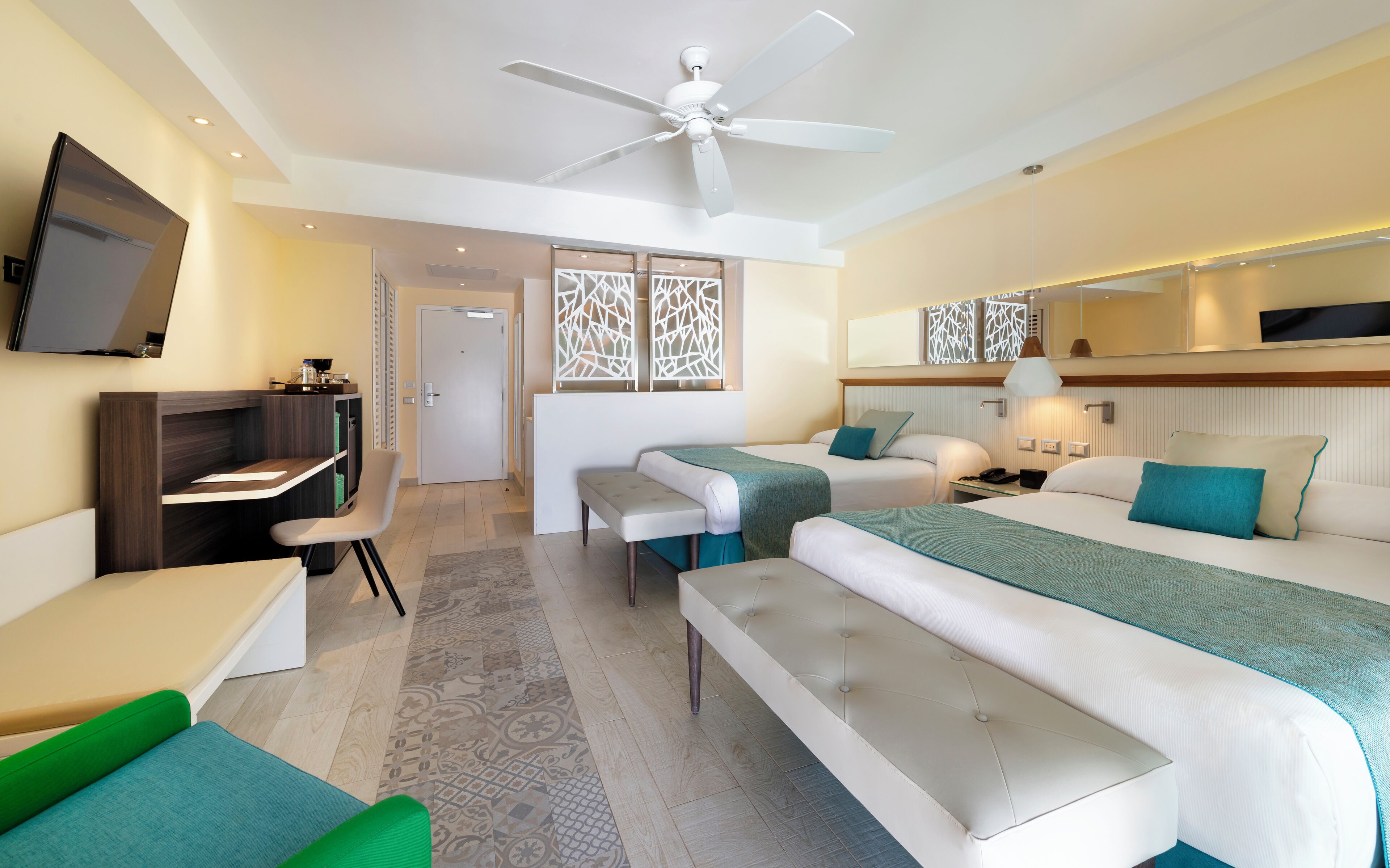 Ein modernes Hotelzimmer mit Bett, Schreibtisch, Sessel, Sofa und Deckenventilator.