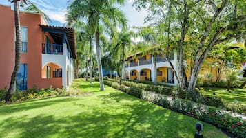 Um jardim bem cuidado, com palmeiras e um caminho que leva a um edifício com varandas.