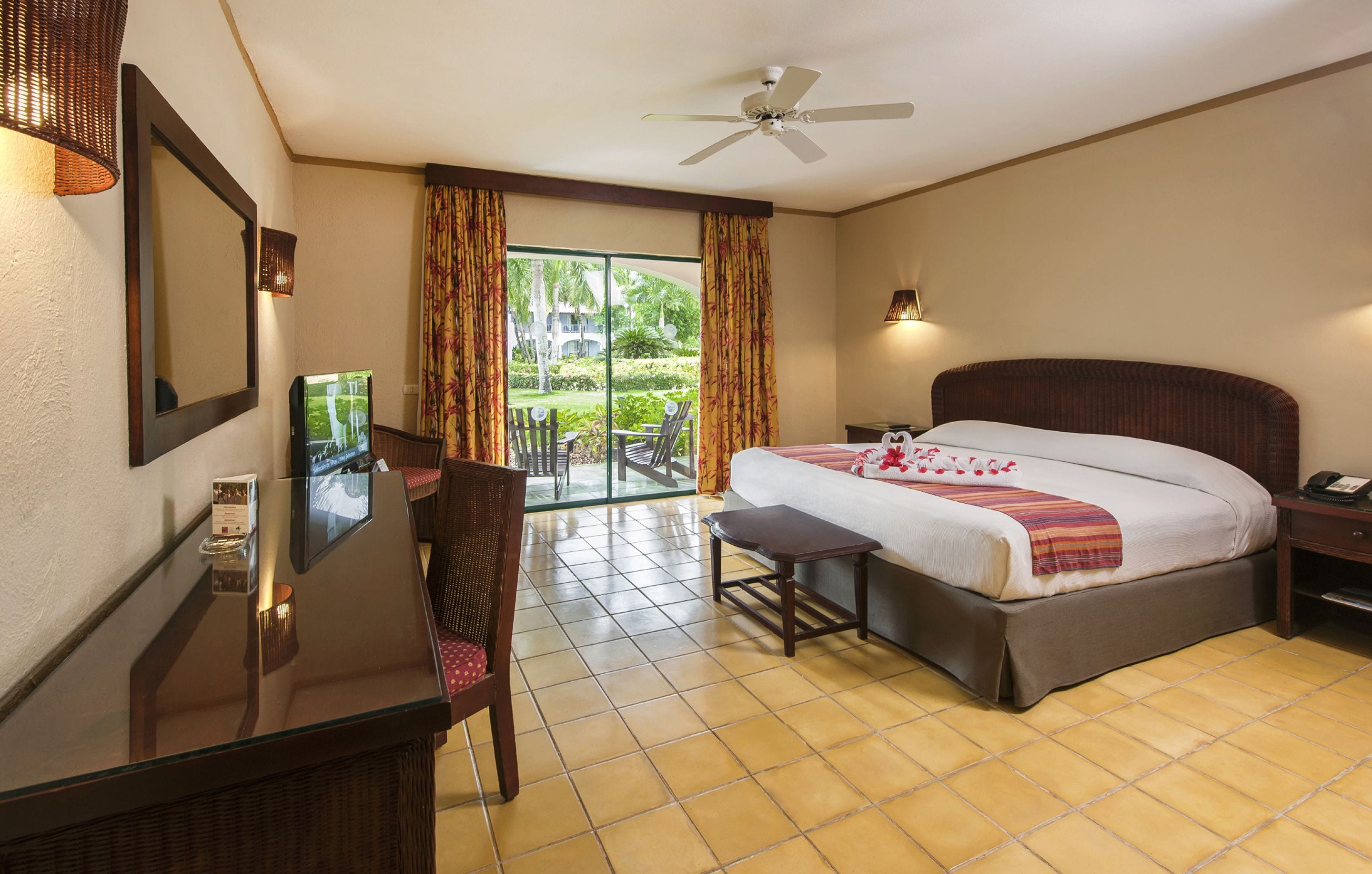 A hotel room with a bed, a desk, a chair, a TV, and a balcony with curtains.