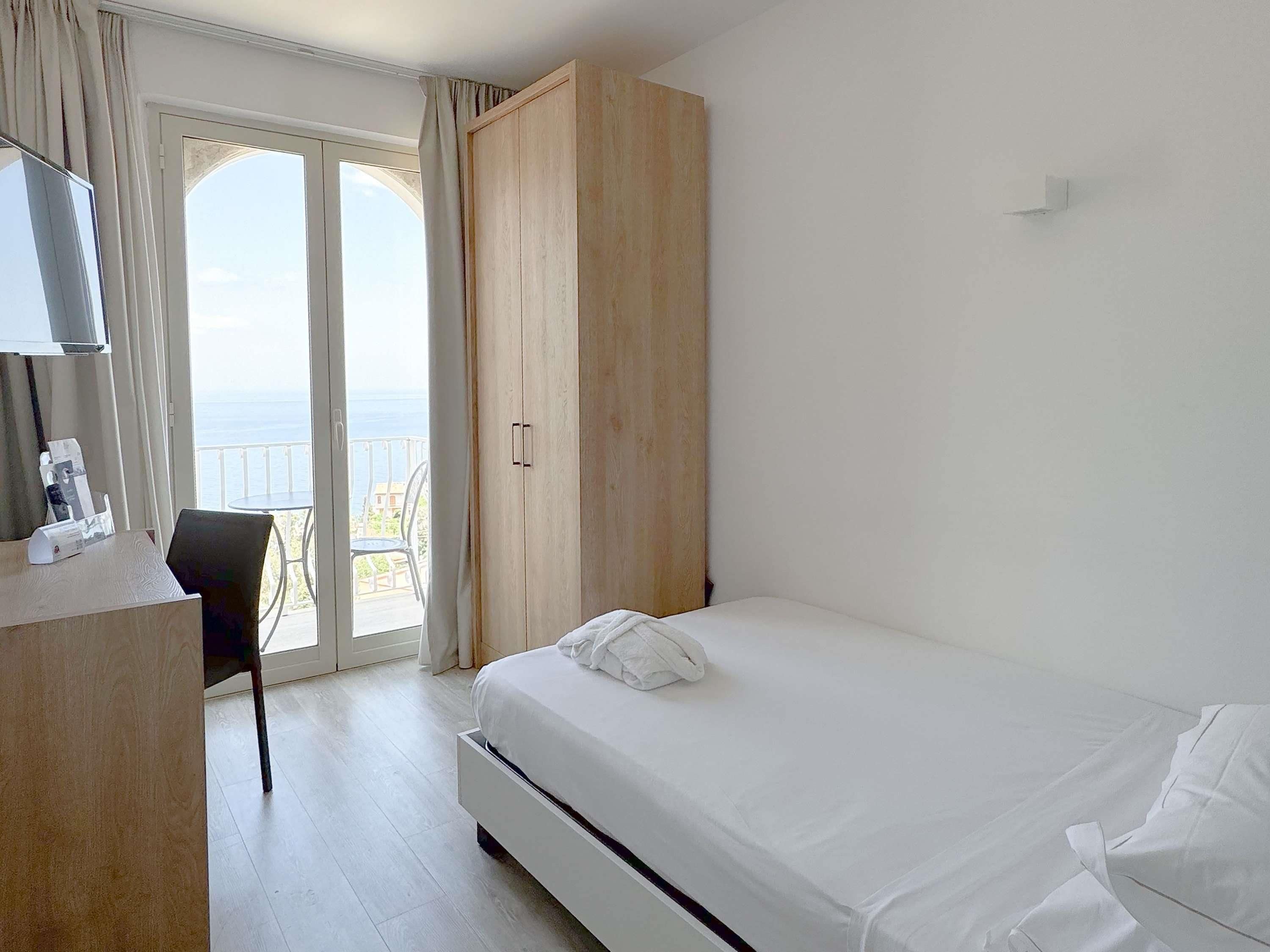 A hotel room with a bed, a desk, a chair, a wardrobe, and a balcony with a view.