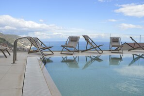 Zona de piscina con sillones de descanso y vista al mar.