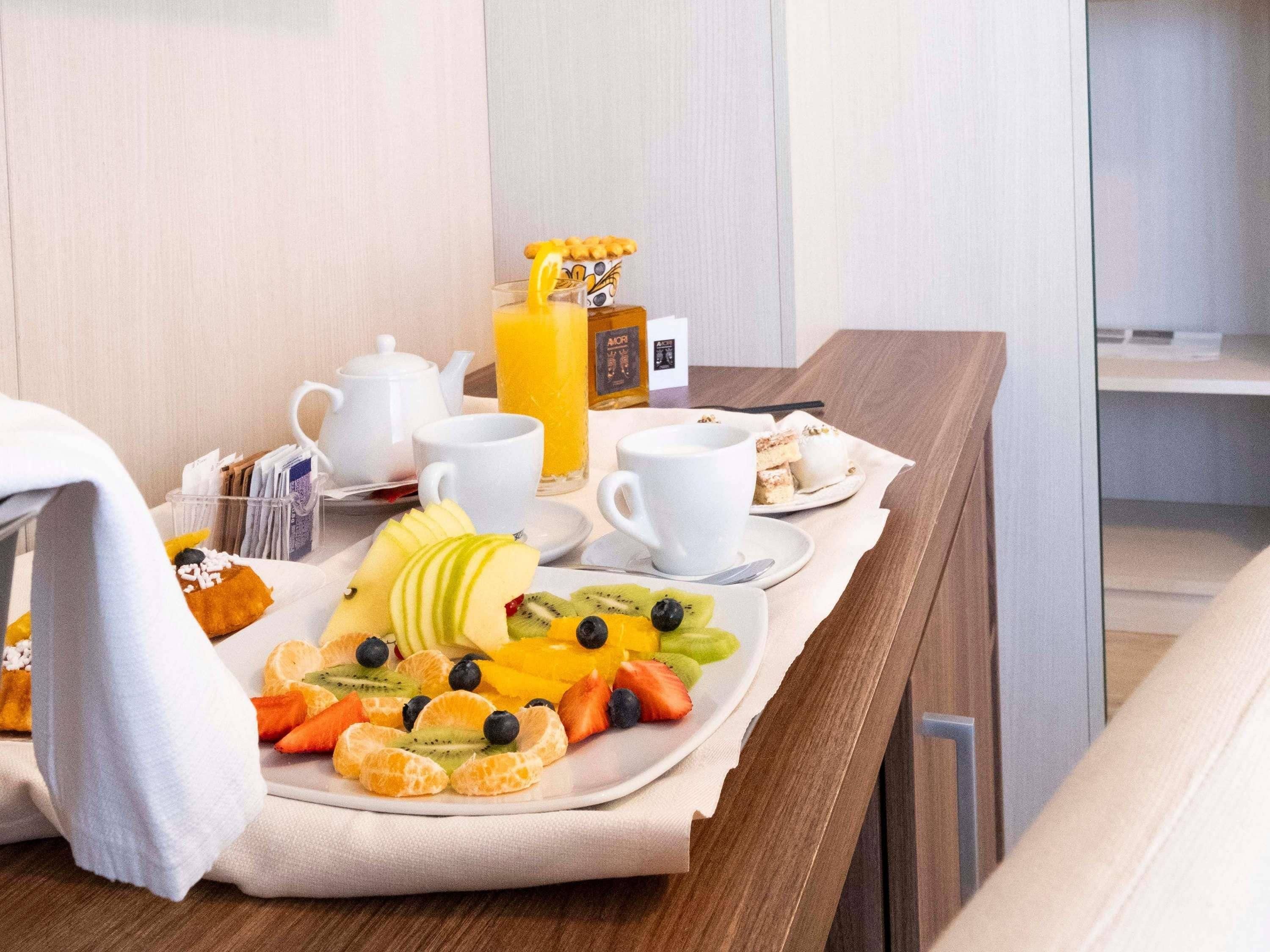 A breakfast setup with a fruit platter, coffee cups, a teapot, and a juice box on a wooden table.