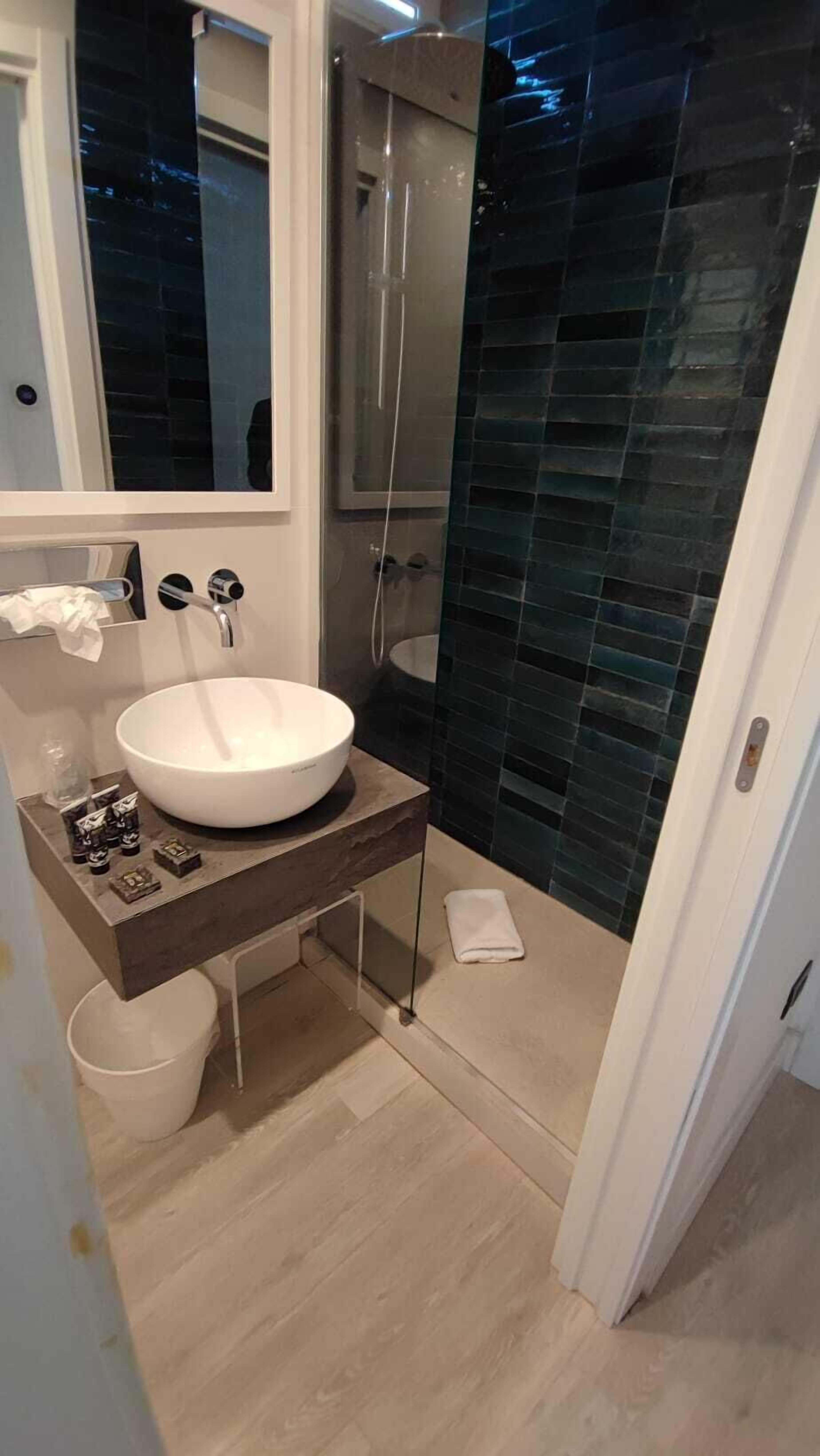 A modern bathroom with a white sink, a glass shower enclosure, and a dark tiled wall.