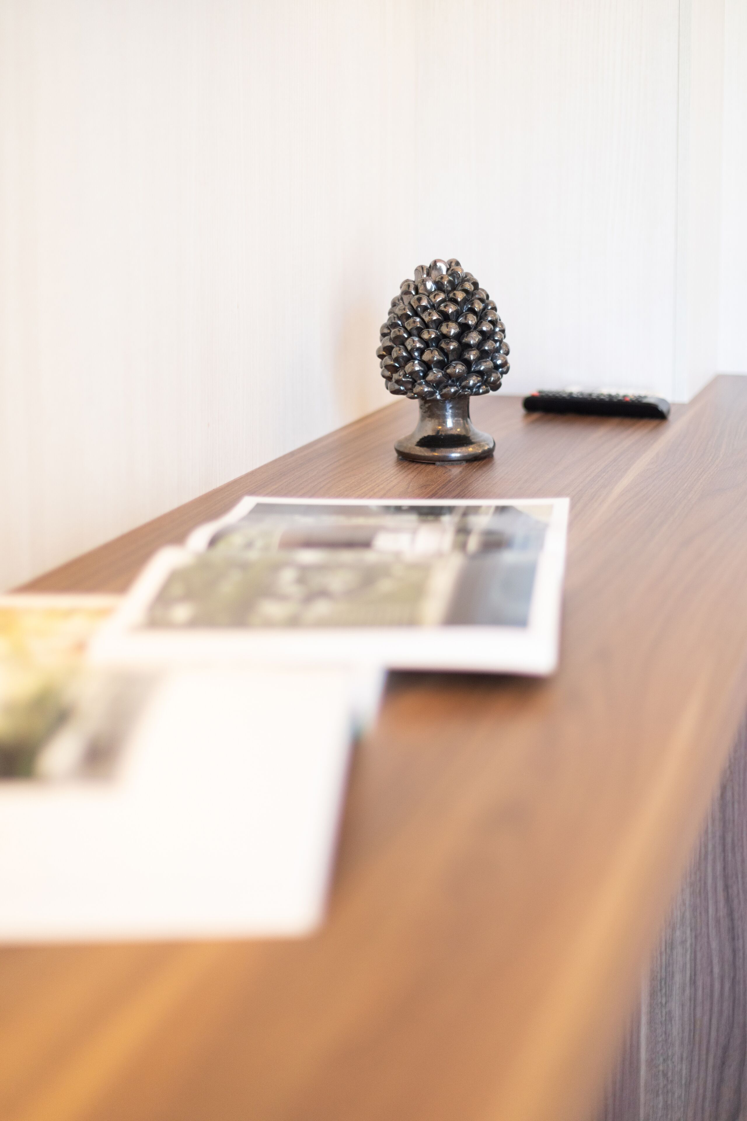 A wooden table with a decorative pine cone ornament and a remote control.