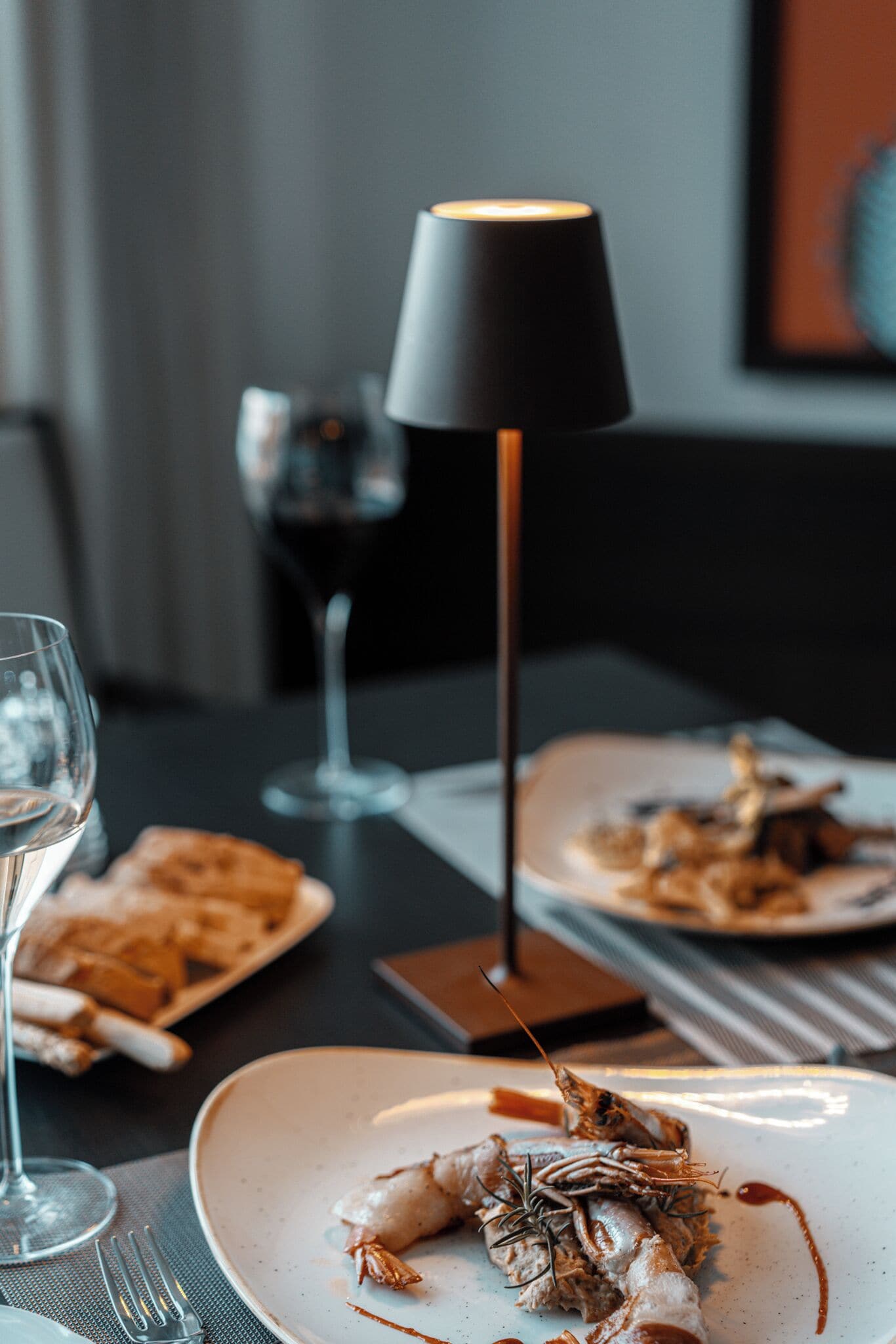 A dining table with plates of food, a wine glass, and a lamp.