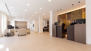 Um lobby moderno de hotel, com balcão de recepção, área de estar e espaço para refeições.