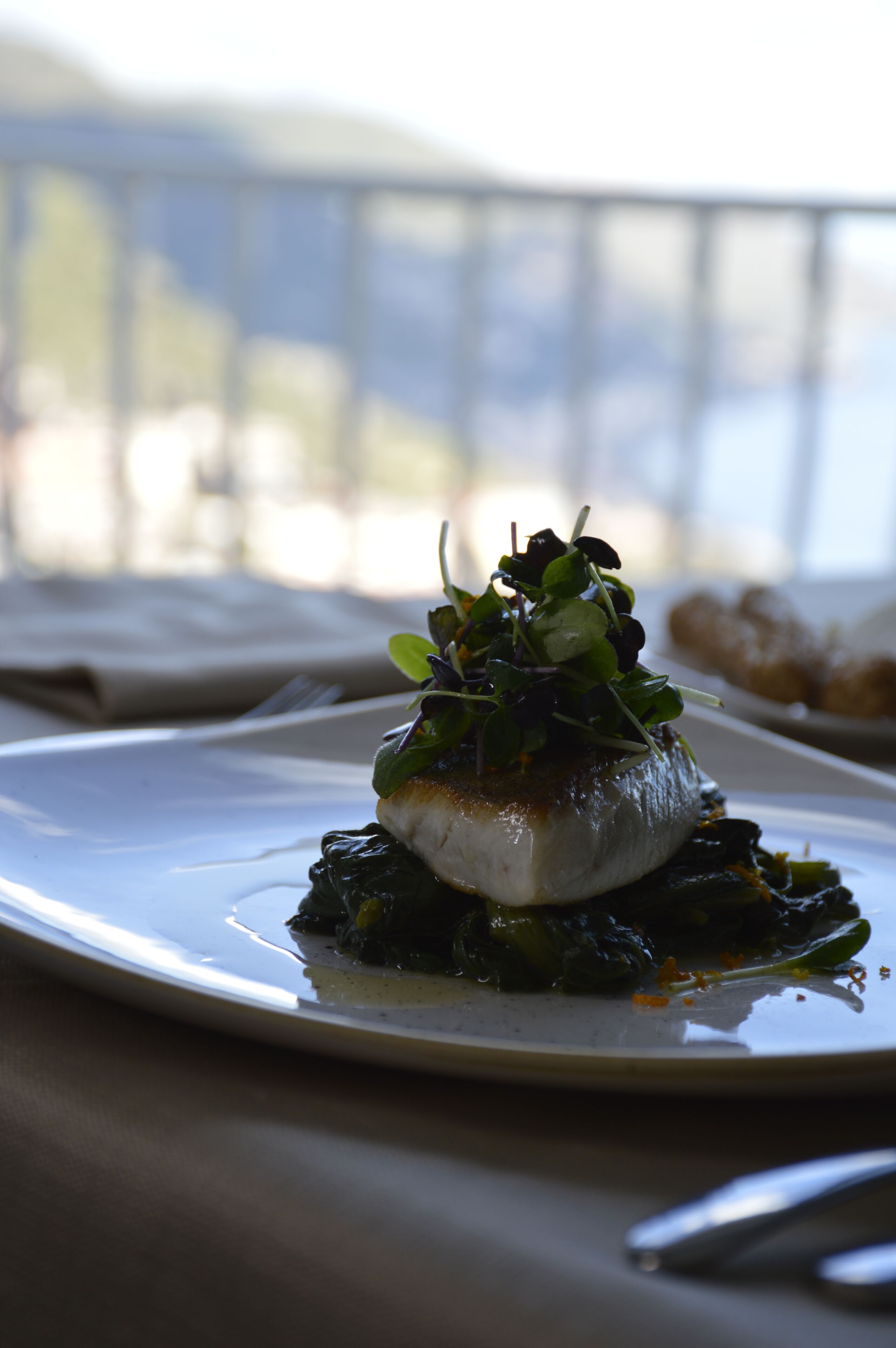 A plate of food with a white base and green garnish, set on a table with a blurred background.