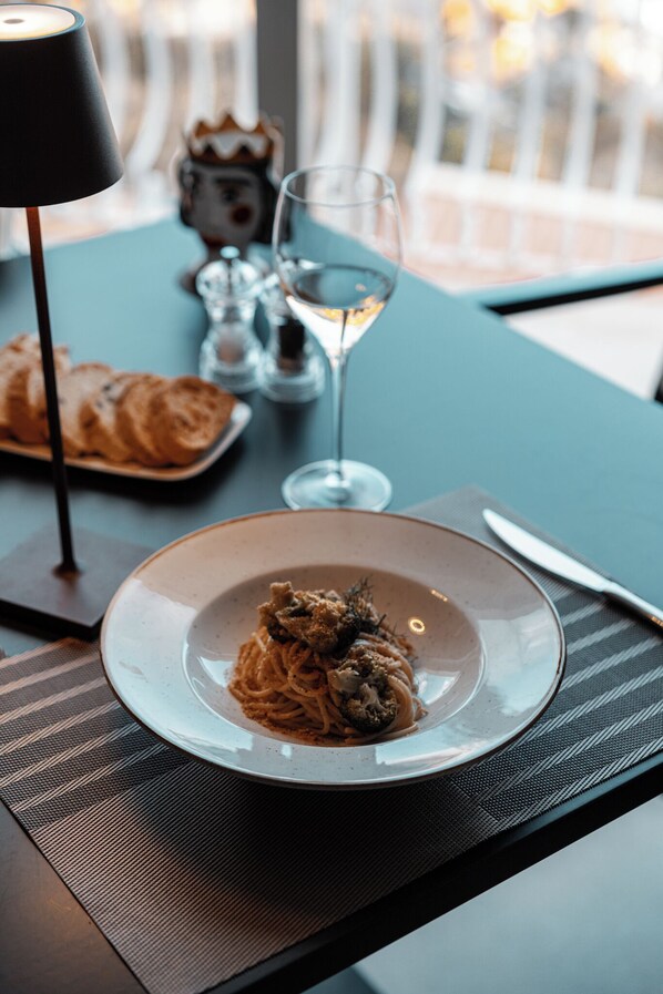 A dining table with a plate of spaghetti, a wine glass, and a lamp. - Splendid Hotel Taormina - Handwritten Collection (Taormina)