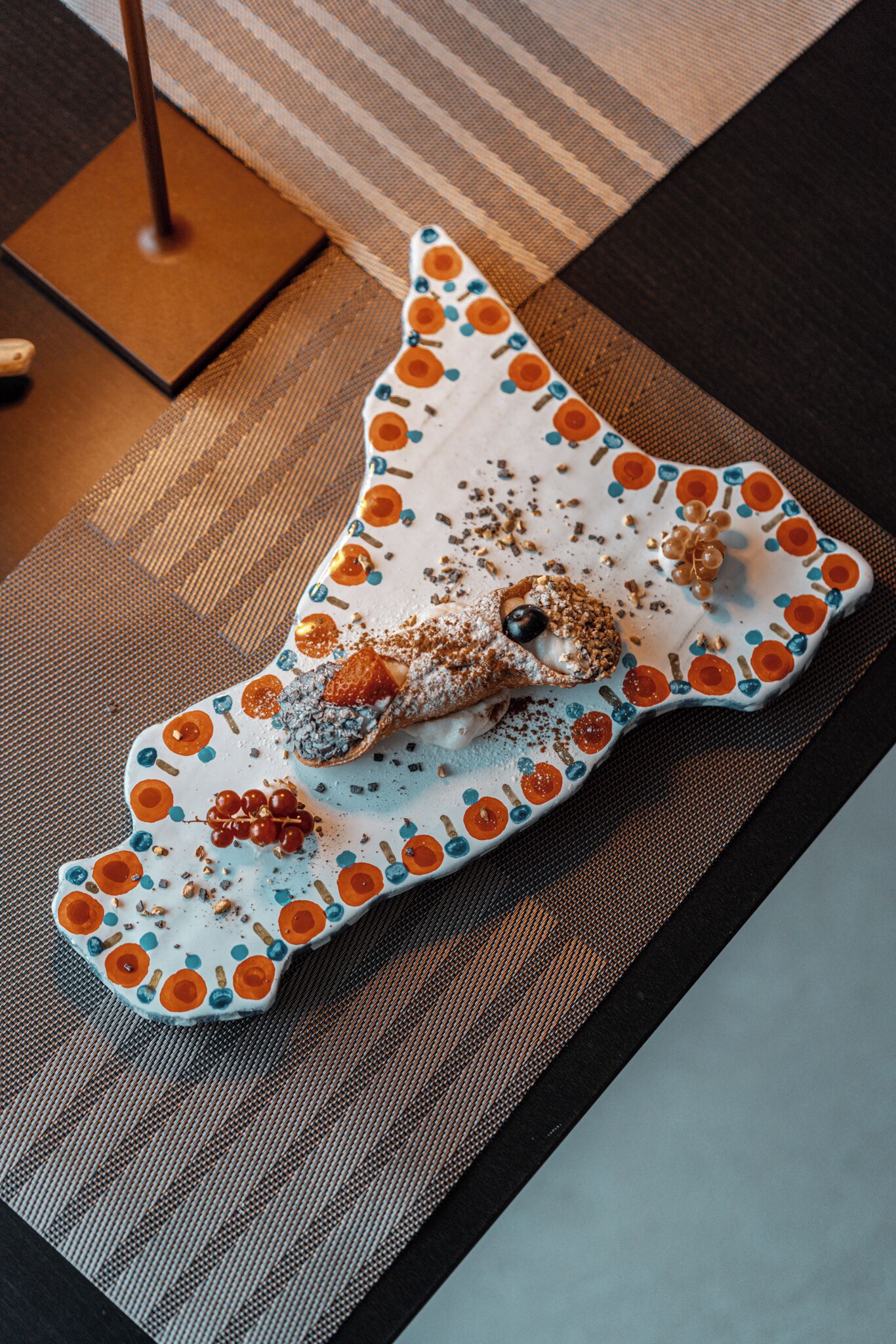 A uniquely shaped plate with a dessert on it, placed on a textured mat.