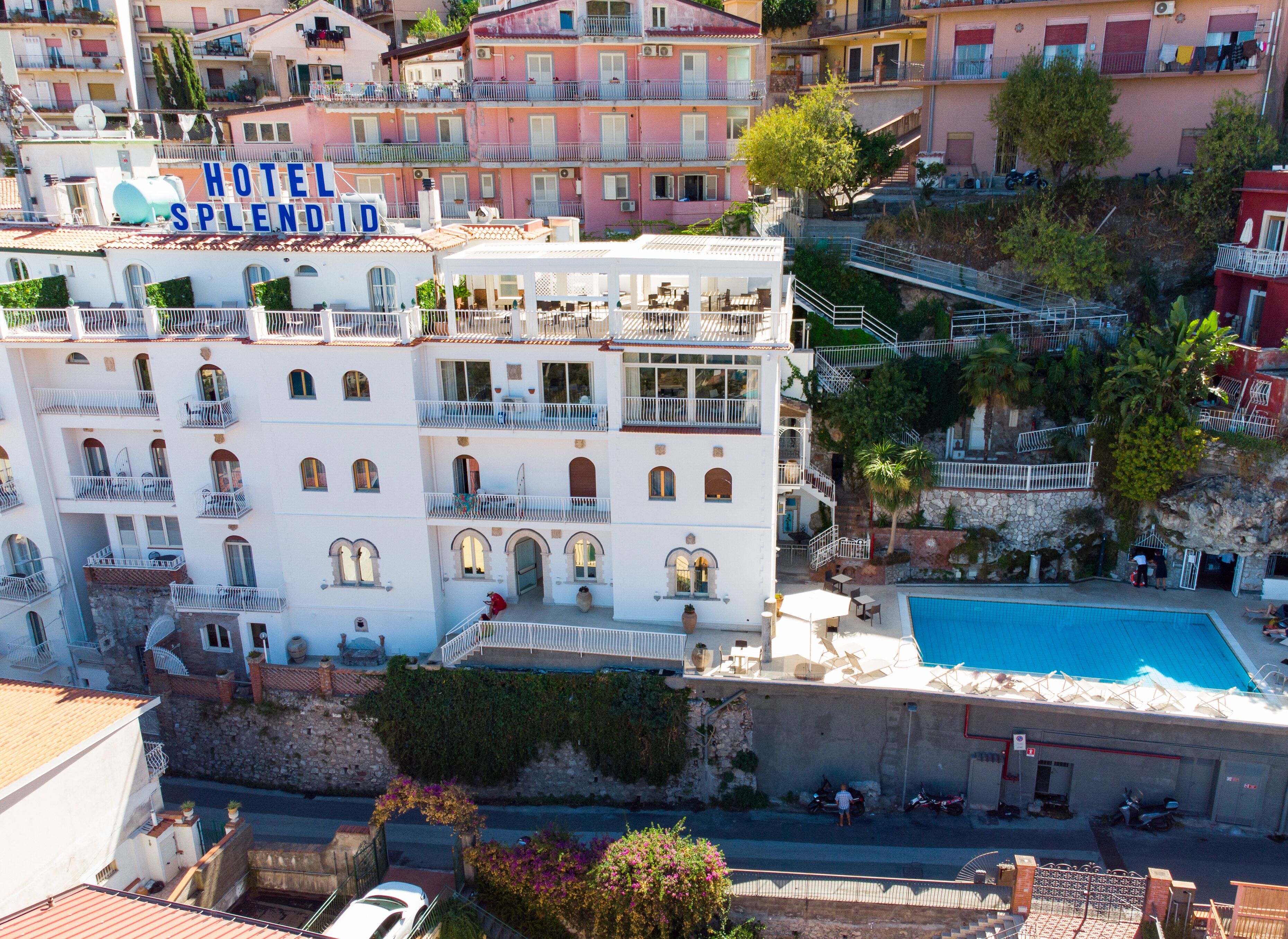 Ein mehrstöckiges Hotel mit Balkonen, einem Schwimmbad und Blick auf die umliegenden Gebäude.