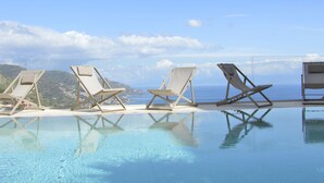 Uma piscina infinita com água azul cristalina e vista para o oceano. Há cadeiras de descanso dispostas ao longo da borda da piscina.