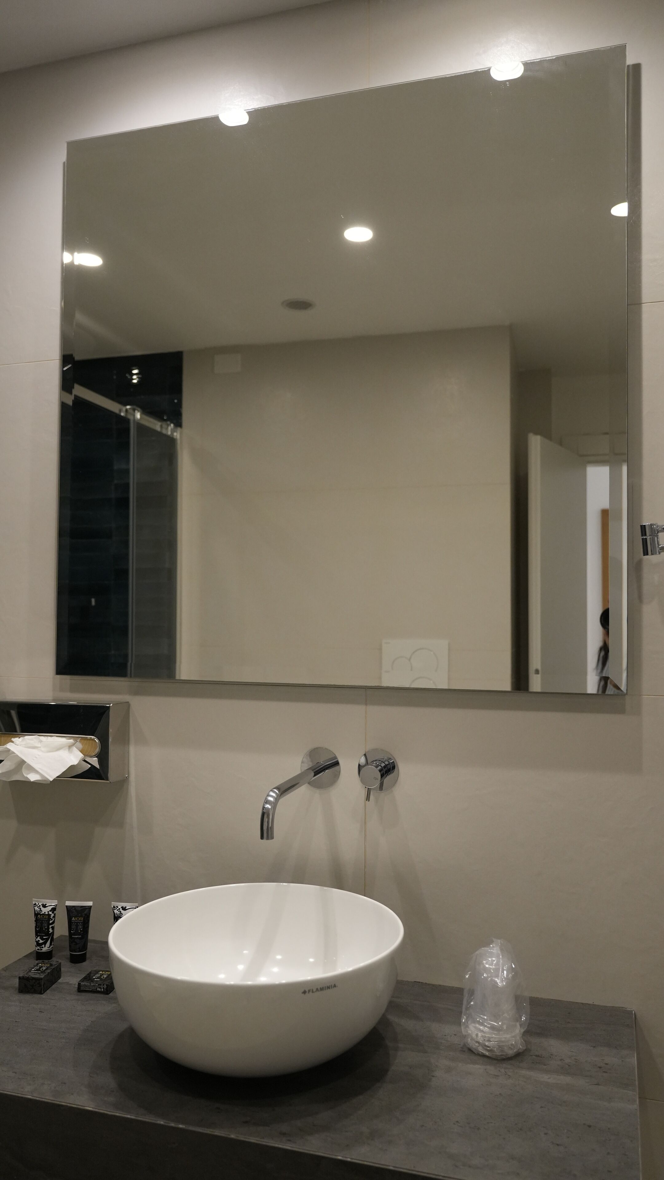 A bathroom with a white sink, a large mirror, and a towel dispenser.