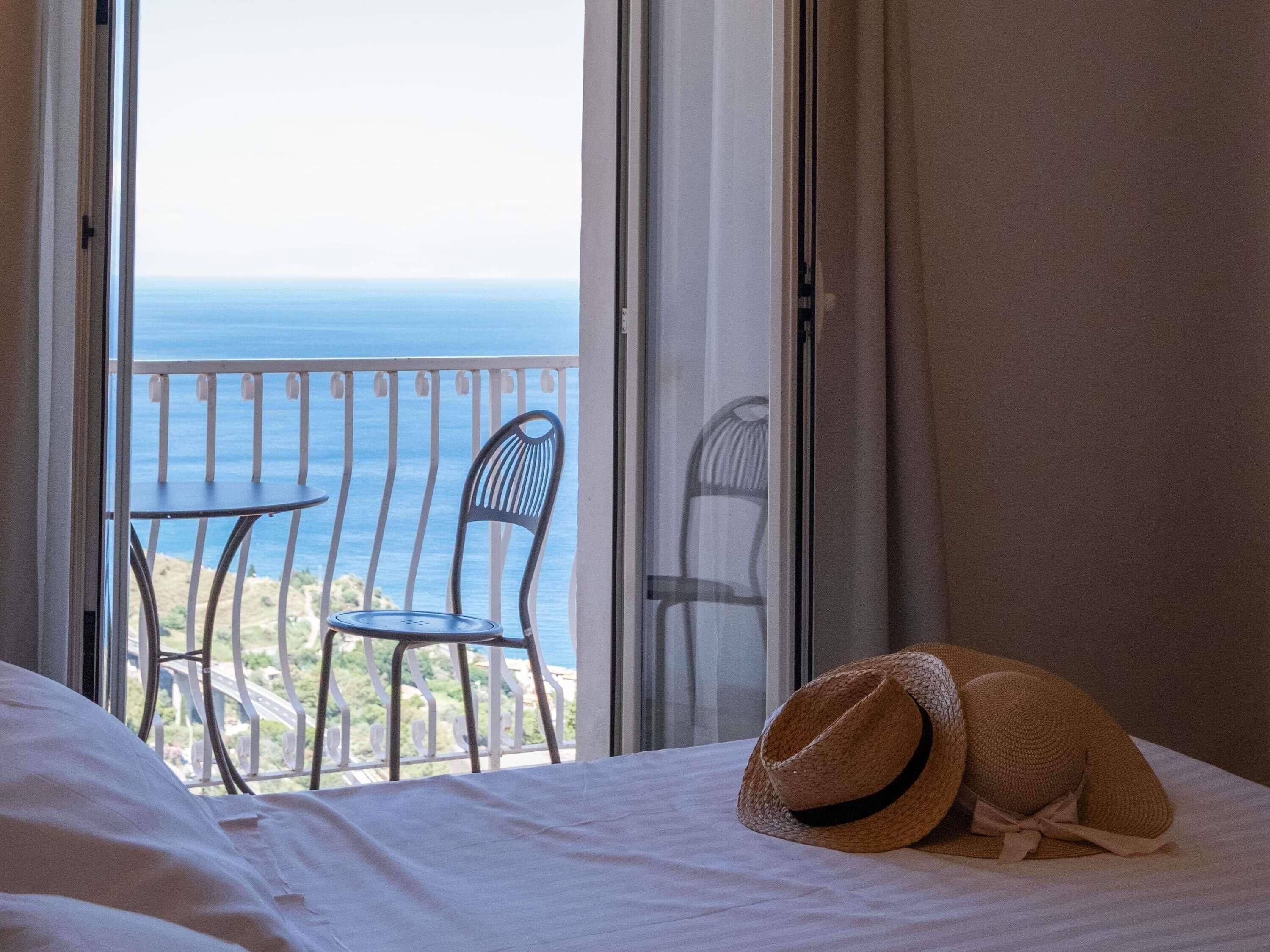 A hotel room with a bed, two chairs, and a view of the sea.