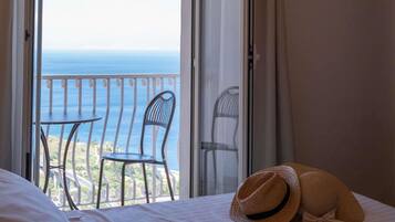 A hotel room with a bed, two chairs, and a view of the sea.