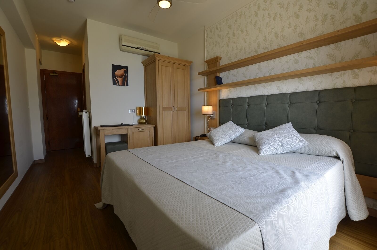 A bedroom with a large bed, a desk, a wardrobe, and a nightstand.