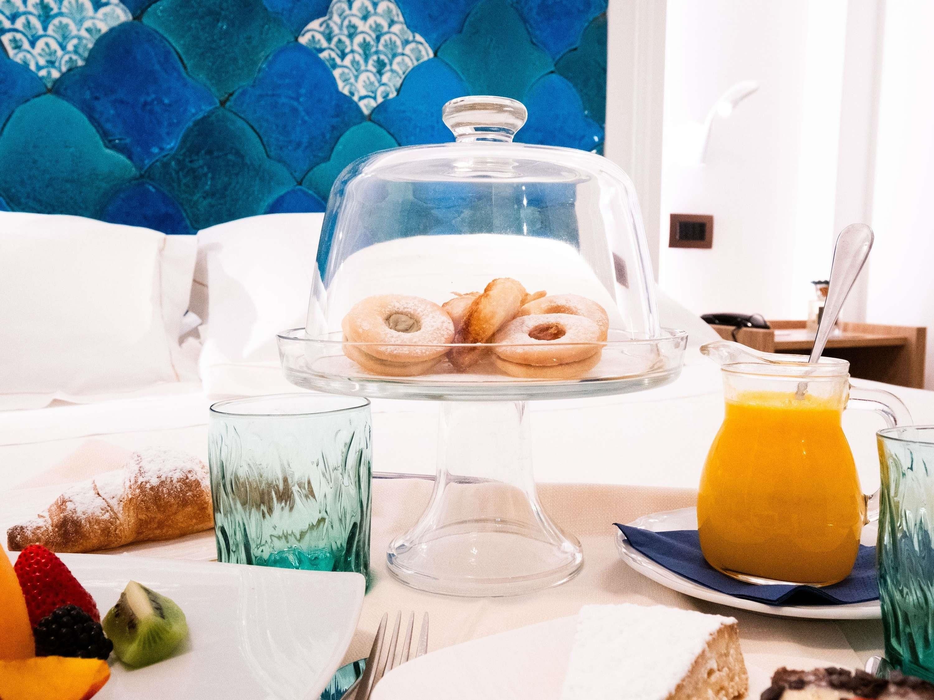 A breakfast setting with a glass-covered pastry display, a fruit plate, and a glass of orange juice.