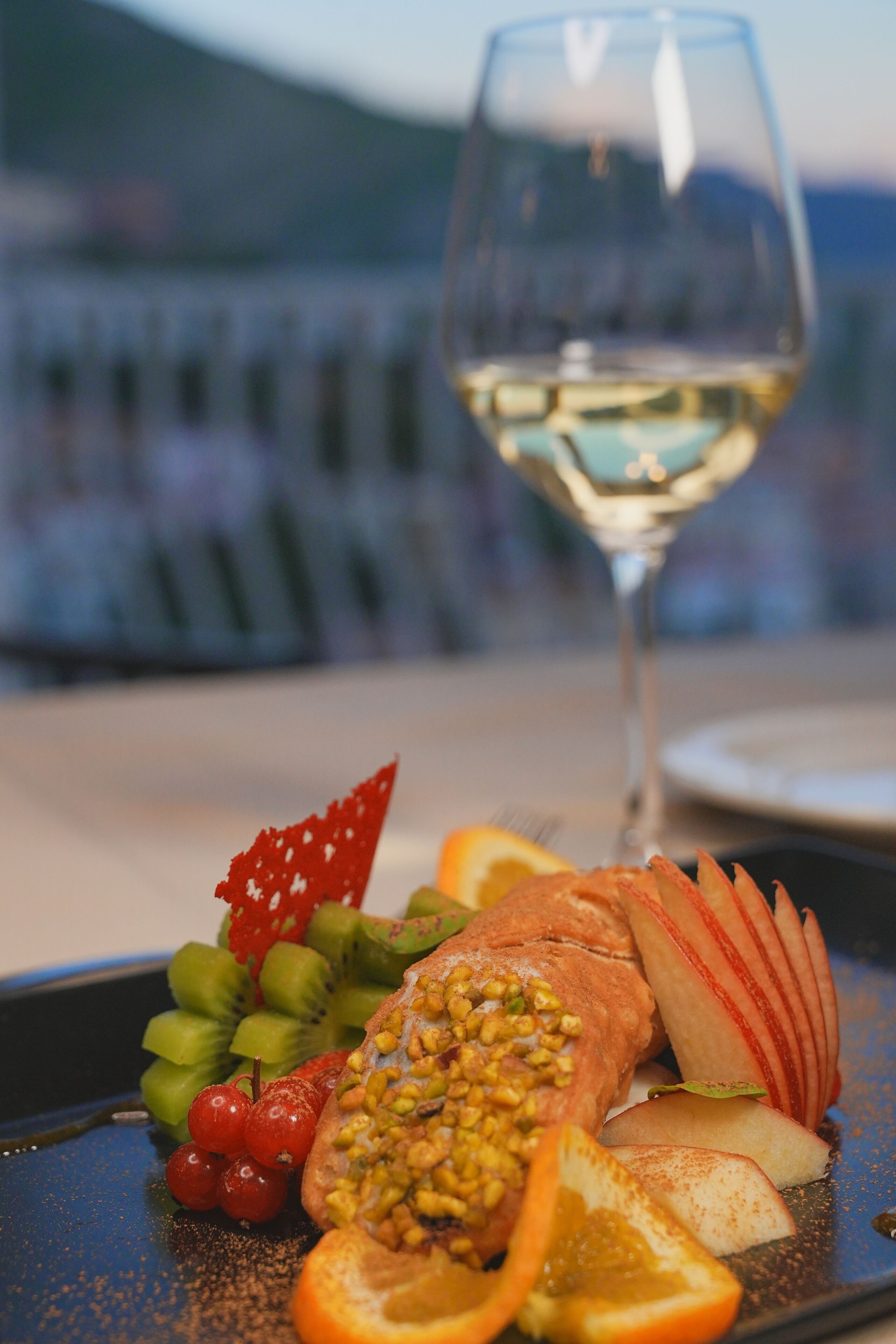 A meal with salmon, fruits, and a glass of white wine on a table with a blurred background.
