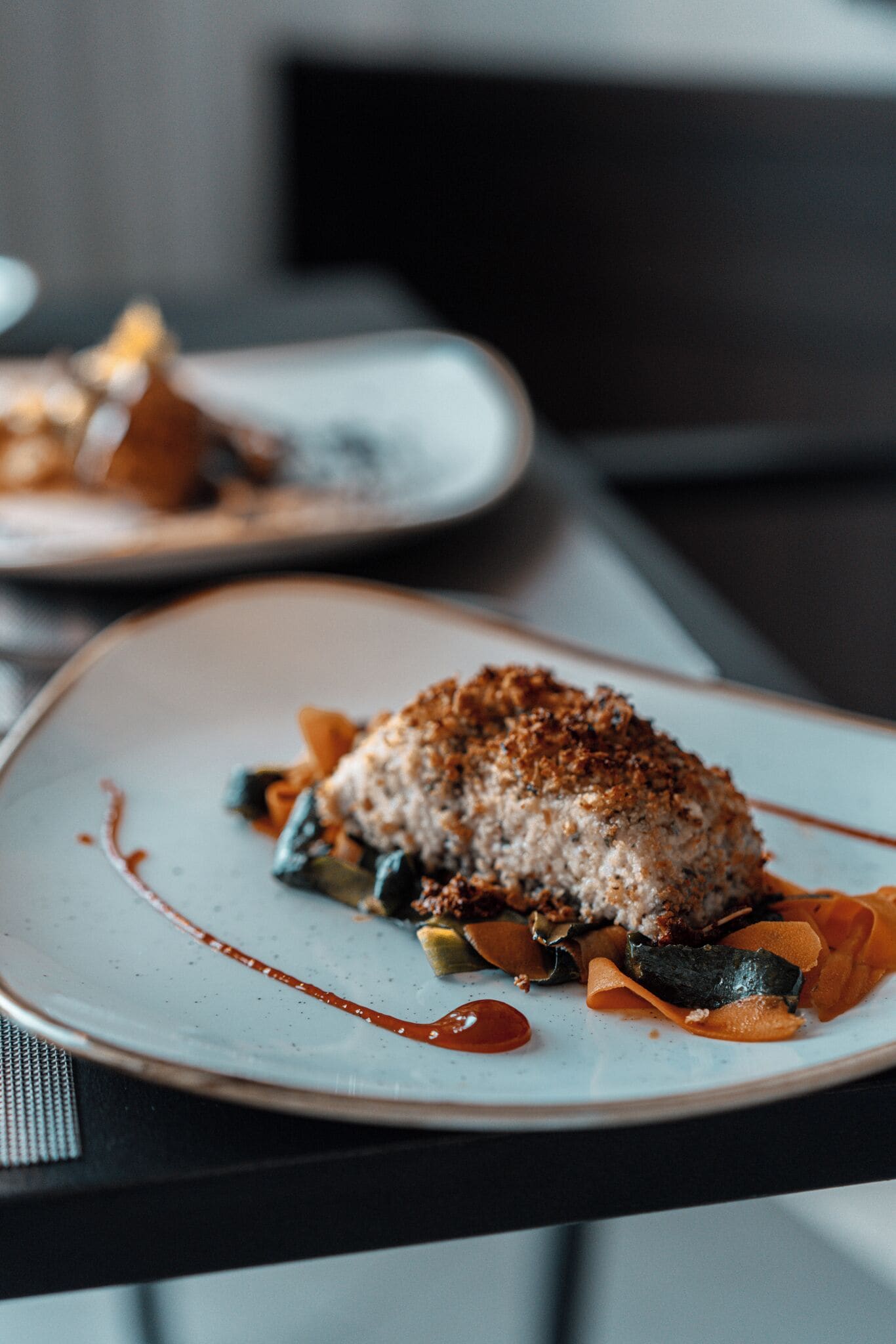 A plate of food with a piece of meat topped with a crispy coating, accompanied by vegetables and sauce.