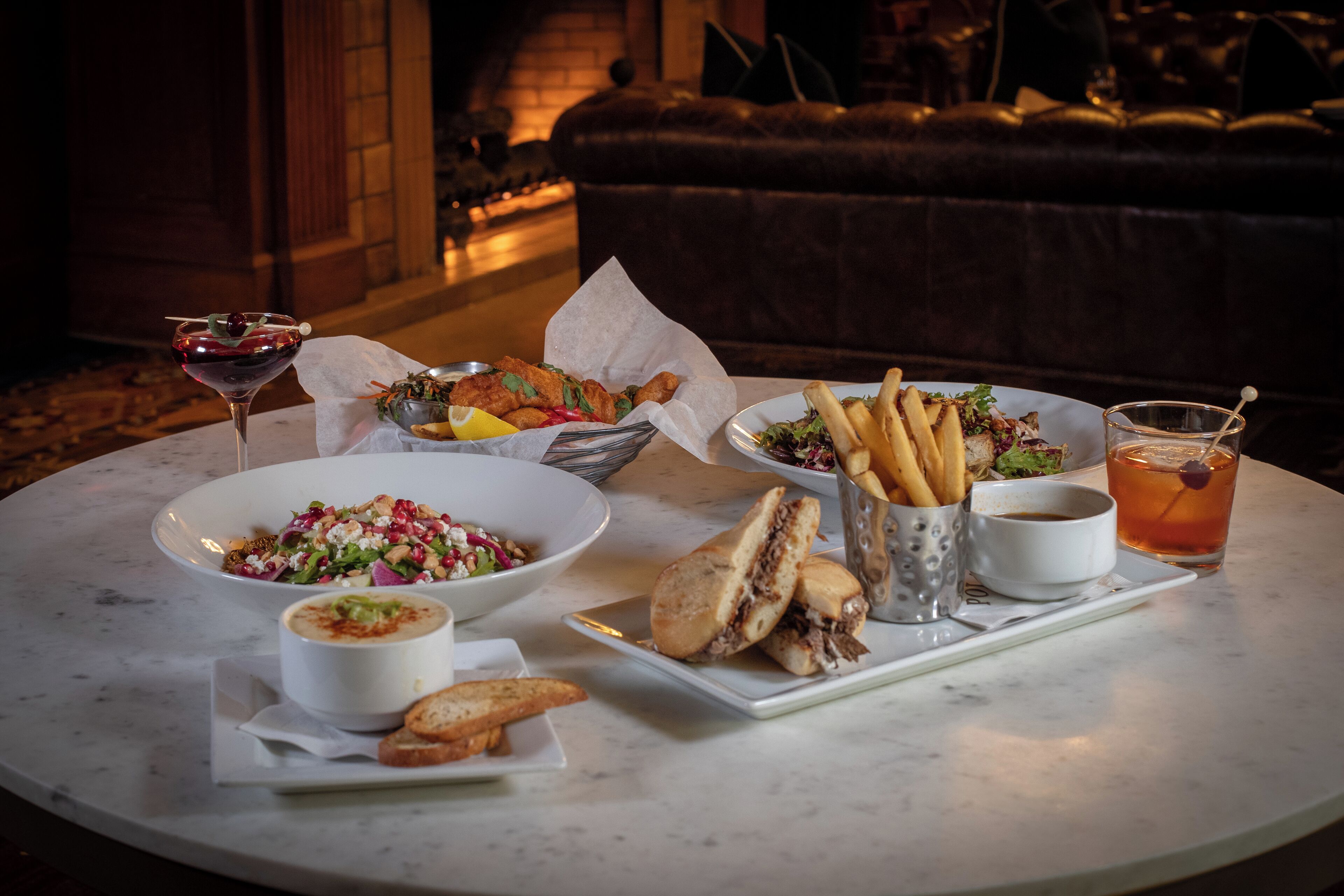 A dining table with various dishes including a salad, soup, sandwiches, fries, and a drink.
